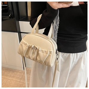 Detailed side view of beige pleated crossbody pillow bag with silver hardware on a model