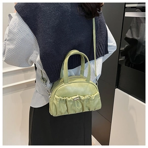 Detail of matcha green pleated crossbody bag styled with navy vest and striped shirt