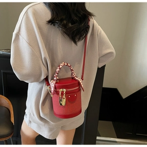 Macro detail of red cylinder bucket bag with woven texture and scarf-wrapped handle