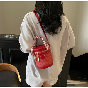 Detail of red cylindrical woven bag with silk scarf handle and golden zipper hardware