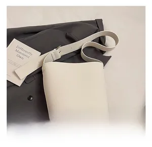Detail der cremeweißen Leder-Beuteltasche mit verstellbarem Gurt über einem grauen Blazer