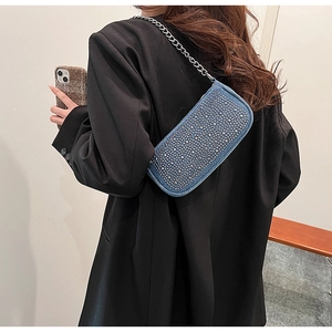 Denim underarm bag with silver studs and chain strap shown on model's shoulder