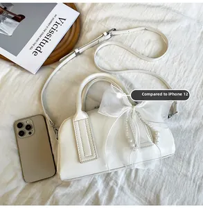 Sac Boston beige chic avec nœud en dentelle et breloque perle à côté d'un smartphone