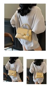 Detail of creamy yellow leather handbag with top handle and heart-shaped leather charm