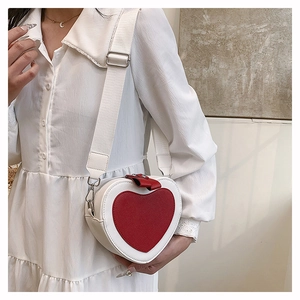 Detail of heart-shaped crossbody bag with red contrast bow and wide canvas strap