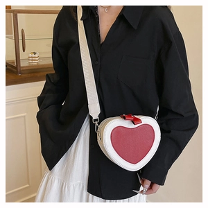 Detail of red and white heart-shaped crossbody bag with adjustable wide strap and bow