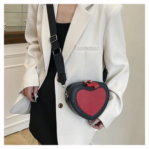 Detail of red and black heart-shaped crossbody bag worn over a white blazer