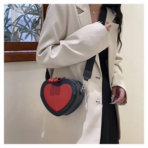 Detail of a heart-shaped crossbody bag with red bow accent and contrast wide shoulder strap