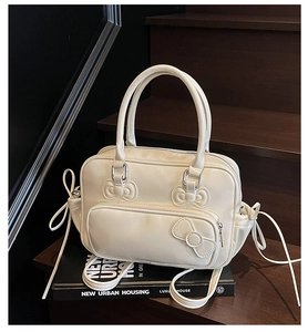 Detail of cream white faux leather bag featuring decorative bow stitching and side drawstrings