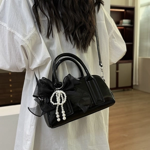 Détail du sac en cuir verni noir avec nœud en résille et pendentif en perles