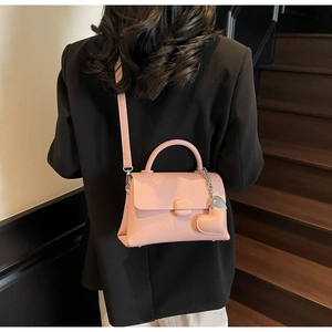 Rear view of a model wearing a pink litchi grain handbag with a heart charm detail