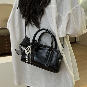 Détail du sac Boston noir brillant avec nœud en maille décoratif et pendentif en perle
