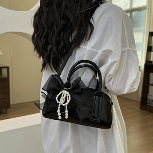 Détail du sac Boston en cuir verni noir avec nœud en maille et perles porté par un mannequin