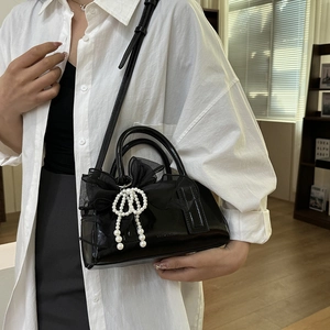 Détail du sac Boston en cuir verni noir brillant avec nœud en dentelle et perle