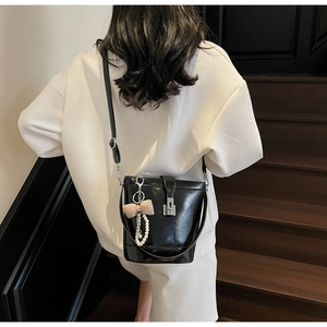 Detail of glossy black bucket bag featuring silver metal buckle and pearl charm accessory