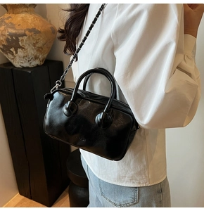 Detail of a black glossy leather Boston bag with a chain strap in a studio setting