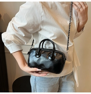 Detail of glossy black leather bowling bag with silver chain strap and top handle