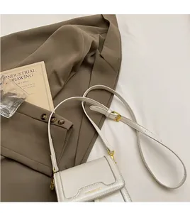 Detail of a minimalist white crossbody flap bag with gold hardware on a dark suit background