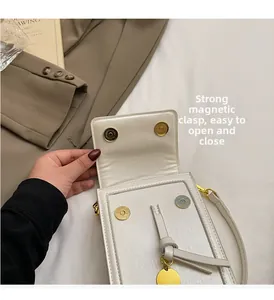 Detail of white leather phone bag with dual gold magnetic buckles and round pendant