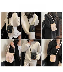 Crossbody phone bag with gold pendant detail, shown in black and beige on a model
