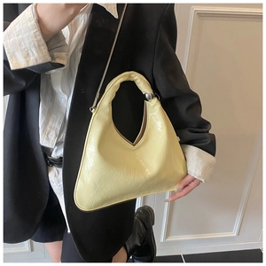 Detail of a creamy yellow triangular handbag with glossy finish and silver metal ball charm