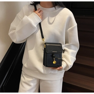 Close-up of black PU leather crossbody phone bag with gold pendant on a white sweater