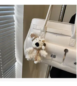 Detailed view of a white plush bear charm with a knitted hat hanging on a leather handbag