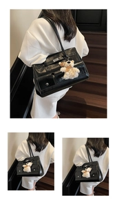 Macro detail of black glossy leather tote bag featuring a metal twist lock and bear charm