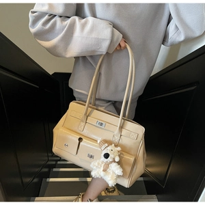 Detail of glossy beige patent leather tote bag with flap pockets and plush bear charm