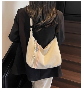 Detail of cream white PU tote bag with woven pendant charm worn over a black blazer