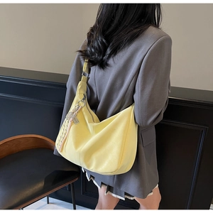 Detail view of a large pale yellow leather hobo bag with wide shoulder strap and charm