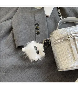 Detail of white fluffy keychain with large black eyes hanging on a woven texture bag