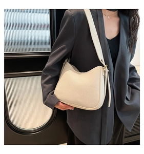 Gros plan d'un sac hobo en cuir grainé blanc crème porté sur un blazer gris