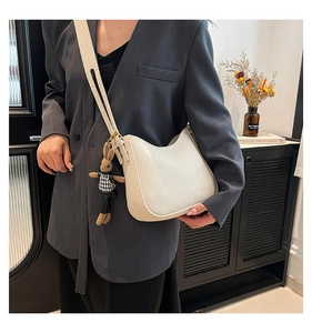 Close-up of white pebble leather half-moon bag with cute brown rabbit charm on wide strap