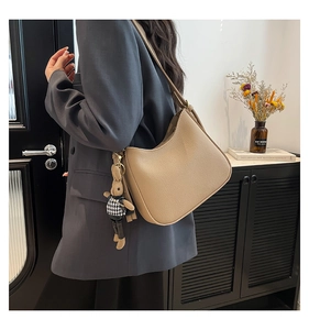 Détail du sac beige en forme de croissant avec texture grainée et pendentif lapin