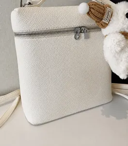 Detalle de bolso en cuero granulado blanco crema con colgante de peluche y cremallera plateada