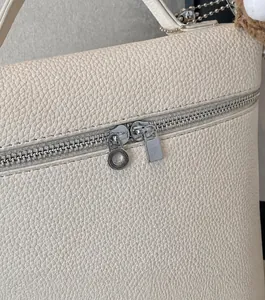 Detalle de cremallera plateada en bolso de cuero blanco crema con colgante de peluche