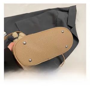 Detail view of beige bucket bag bottom with silver protective studs and teddy charm