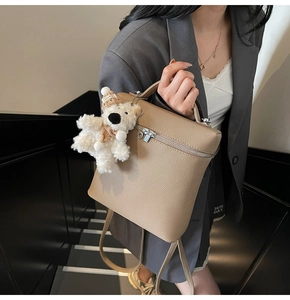 Detalle de la mochila de cuero caqui con textura de grano fino y un tierno colgante de oso