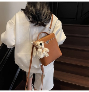 Bolso bandolera de cuero marrón con colgante de osito de peluche blanco en la modelo