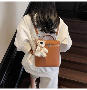 Bolso de mano en cuero marrón con un colgante de oso blanco llevado por modelo