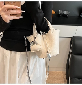 Close-up of white lychee leather bucket bag with silver chain and heart pendant detail