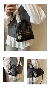 Detail of black glossy handbag with heart charm, metal zipper and detachable strap