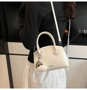 Detailed view of a white shell handbag with glossy finish and heart-shaped charm accessory