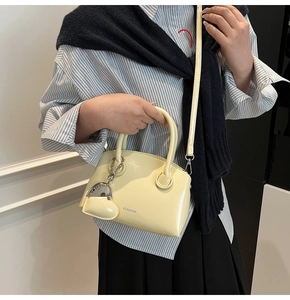 Detail view of cream crossbody bag with silver logo and heart charm on striped shirt