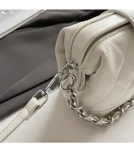 Dettaglio di gancio argentato e catena su una borsa in pelle bianca trapuntata