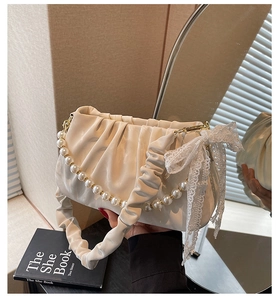 Detail view of cream pleated handbag featuring pearl bead handle and lace bow decoration
