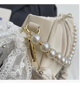 Detail of elegant pleated handbag featuring pearl strap with golden clasp and lace bow