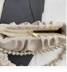 Detail of a smooth golden zipper on a pleated cream handbag with pearl bead strap