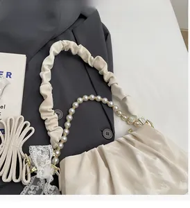 Detail of cream pleated handbag with pearl chain and elegant lace bow accessory